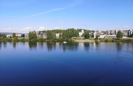 (Illustrasjonsbilde) En elv som renner foran et bysentrum. I bakgrunnen hus og trær. Sol og blå himmel. Glomma og Leiret med rådhuset.