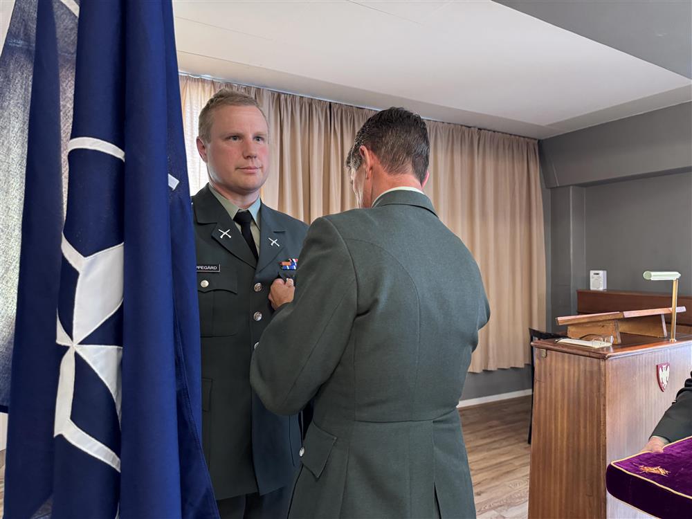 En mann i uniform fester en medalje på brystet til en soldat. - Klikk for stort bilde