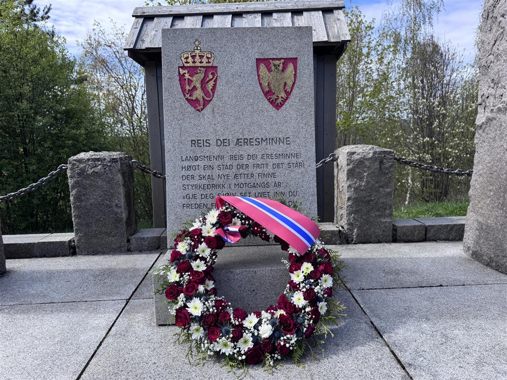 En blomsterkrans ligger foran en minnesstein. - Klikk for stort bilde