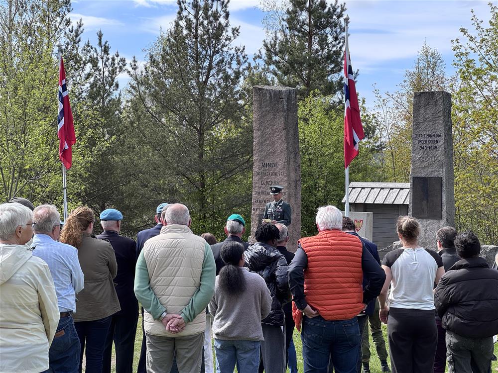 En mann holder tale ved et krigsminnesmerke, folk står foran og hører på. - Klikk for stort bilde
