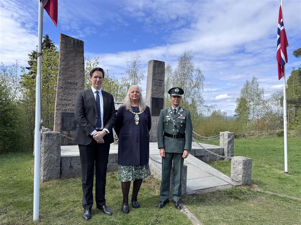To menn og en kvinne står siden av hverandre foran et krigsminnesmerke. - Klikk for stort bilde