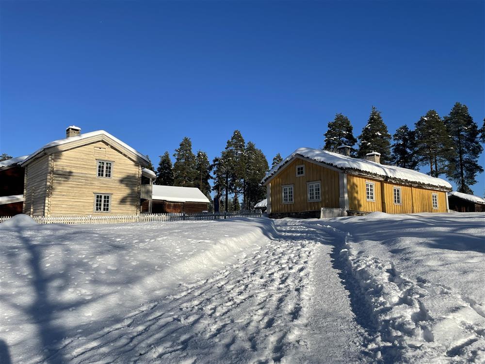 To gule hus om vinteren med en vei som går opp til husene. - Klikk for stort bilde