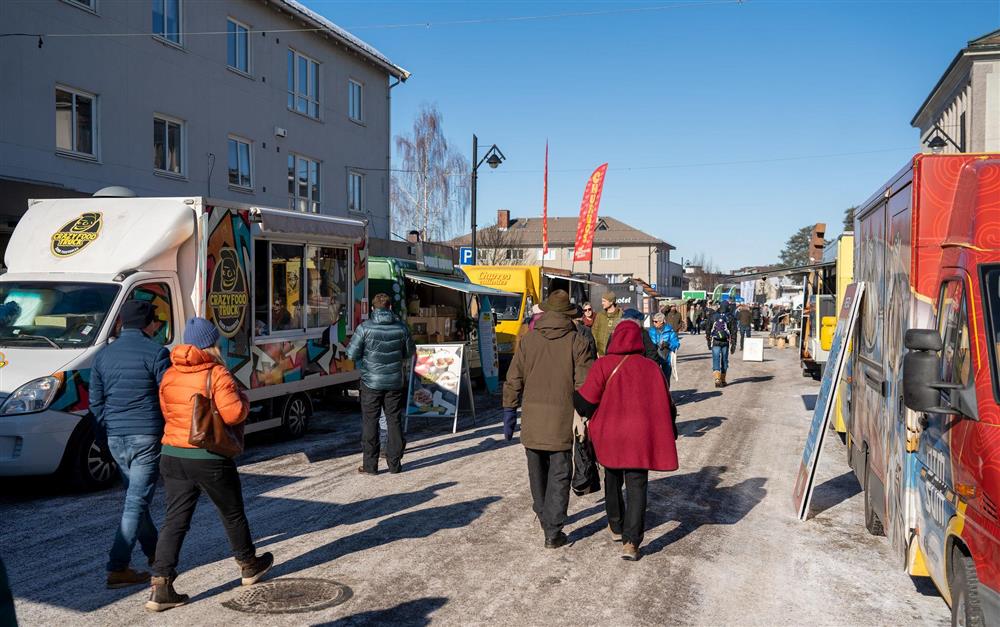 Folk går i en gate med forskjellige boder på hver side av gaten. - Klikk for stort bilde